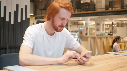Homme rousse tapant un message sur un smartphone dans un café, navigation