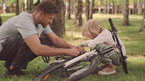 Father and Son Repairing Bicycle Brakes in Park