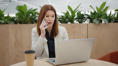 Woman Talking on Phone and Using Laptop in Office