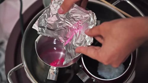 Hand made candles production, female hand adding dye to melting wax in pots. Slow motion