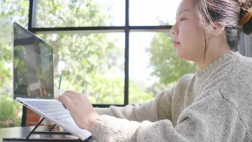 Asian woman typing on laptop and drinking coffee at cafe