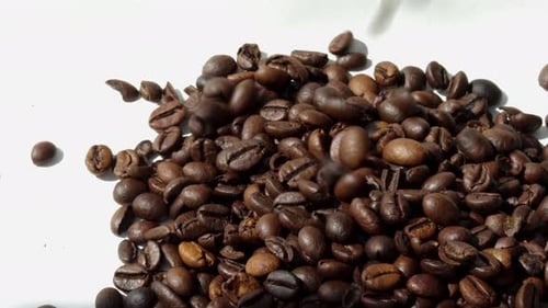 Coffee Beans Falling onto White Surface Close Up