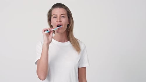 Smiling Woman Brushes Teeth in Bright Studio