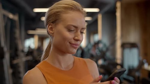 Thinking Athlete Woman Using Smartphone at Gym. Sport Girl Texting in Sport Club