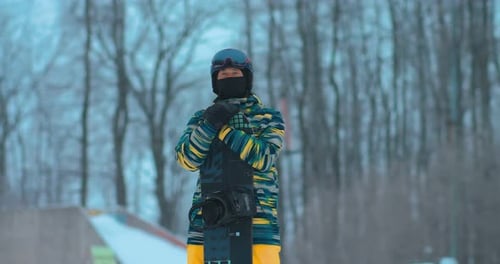 Professional Athlete Stands on a Hill and Looks Into the Distance Holds a Snowboard in His Hands