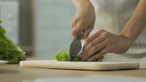 Light-skinned person cutting fresh green lettuce on board