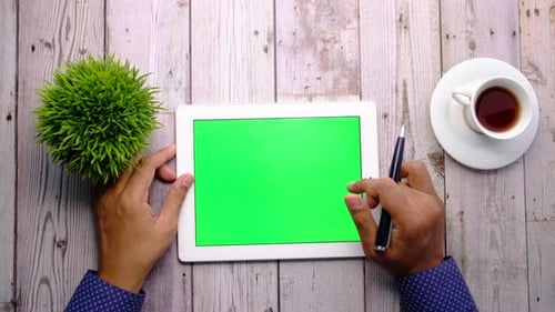 Person Working on Digital Tablet with Green Screen at Office Desk