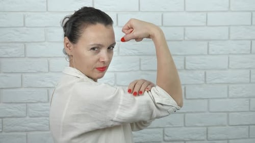 Adult Woman Flexing Arm Muscle by Brick Wall