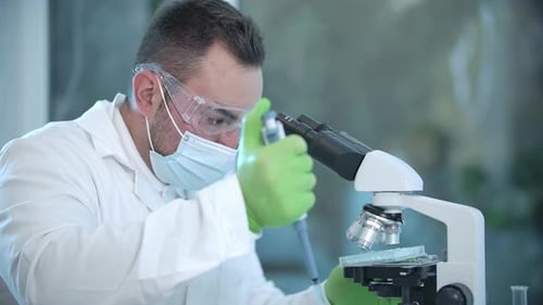 Serious Scientist Using Pipette and Microscope in Lab