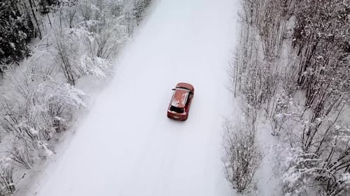Aerial View of a Snowy Forest and Road with a Car in the Winter