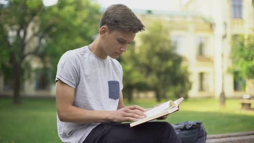 Aufmerksamer Teenager liest Abenteuerbuch auf Bank im Park, Intellektuelles Hobby