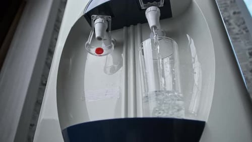 El agua clara se vierte en el vaso desde el enfriador de agua