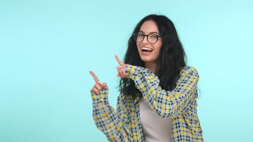 Смешная брюнетка в очках танцует, показывает рекламу и улыбается, показывает пальцем