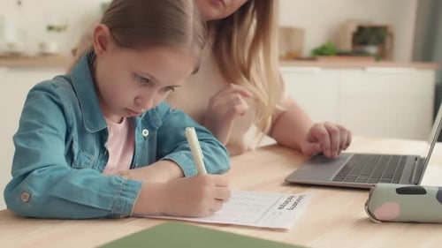 Girl Studies at Table with Mother Using Laptop