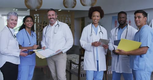 Portrait of diverse male and female doctors standing in hospital corridor smiling to camera