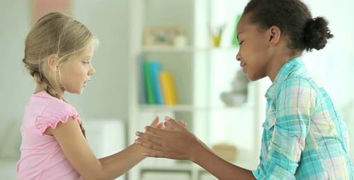 Two Young Girls Playing Hand Clapping Game Indoors