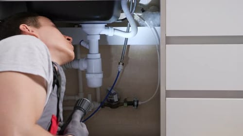 Man with Flashlight Searches Leakage on Pipes and Waste Trap