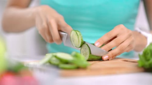 Woman Slices Cucumber on Cutting Board in Kitchen