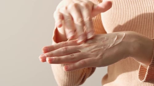 Female Applying Hand Cream Against White Background Close Up