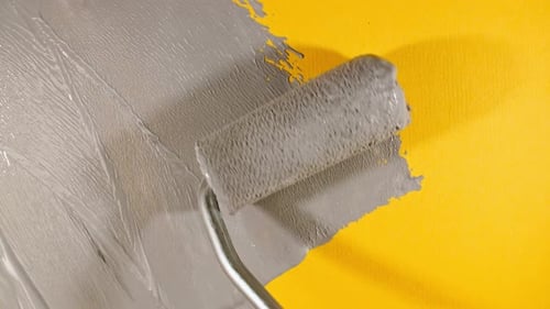 Paint Roller Applying Gray Paint on Yellow Surface