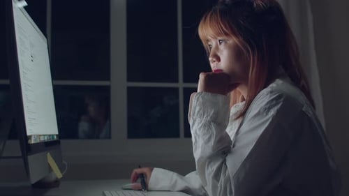 Young asian woman working late using desktop on desk in living room at home