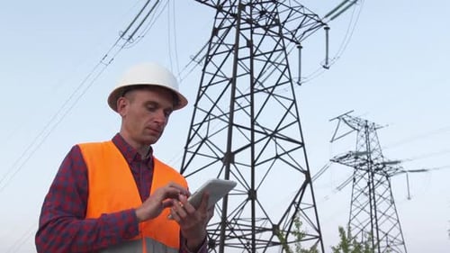 Engineer Using Tablet Near Powerlines on Sunny Day