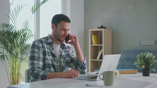 Young Man Working at Home on Laptop and Phone