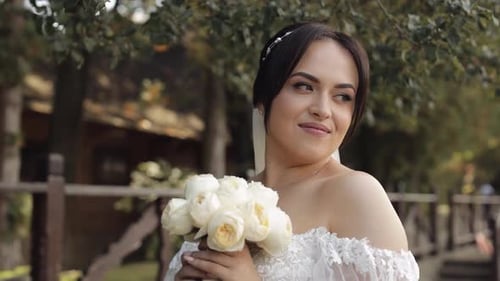 Beautiful Stylish Bride in White Wedding Dress and Veil Holding Wedding Bouquet in Hands in Park