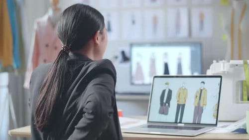Vista posterior de una diseñadora asiática en traje de negocios que tiene dolor de espalda mientras diseña ropa