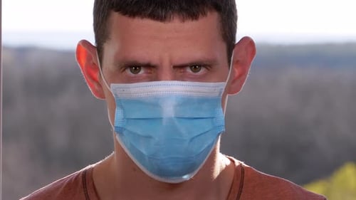 Young Man in a Medical Protective Face Mask Looking at the Camera on the Street Background