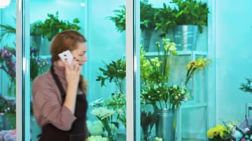 Owner of the Flower Shop Talking on the Phone and Walks Looking Showcase of Flowers