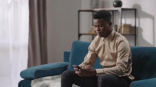 Man using smartphone sitting on modern living room sofa