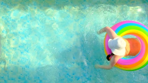 Summer time.Child swims in the swimming pool.Girl in a hat with a rainbow inflatable ring
