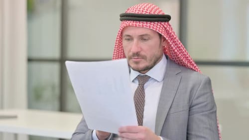 Middle Aged Arab Businessman Reading Reports while Sitting in Office