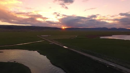 Luftaufnahme, die bei farbenfrohem Sonnenuntergang rückwärts über den gewundenen Fluss fliegt