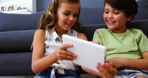 Siblings using digital tablet in living room