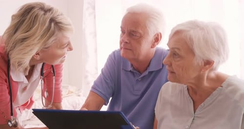 Friendly Doctor Talking with Senior Couple at Home