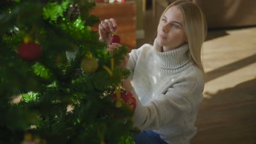 Woman Decorating Christmas Tree with Ornament at Home
