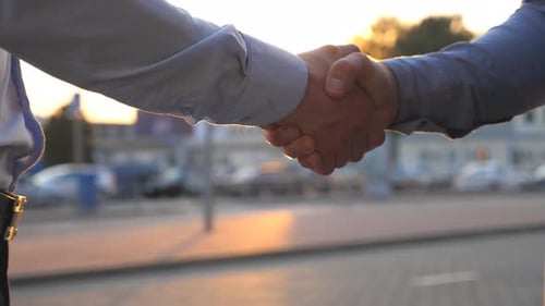 Close Up of Two Successful Businessmen Greeting Each Other Against the Background of Cars Parking