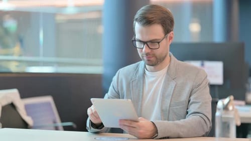 Young Man Celebrates Success Using Tablet at Workplace