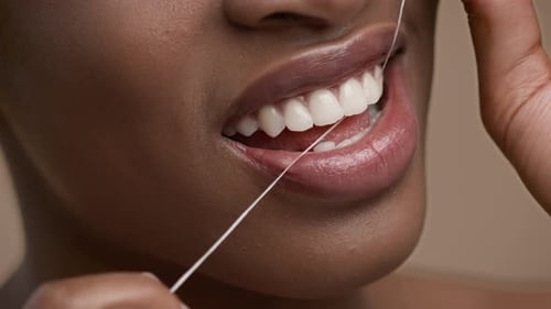 Nahaufnahme einer Afroamerikanerin mit Zahnseide auf beigem Hintergrund