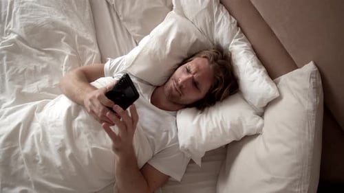 Young Man Using Mobile Phone in Bed