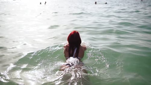View From the Back a Slender Woman in a Swimsuit Swims in the Clear Sea