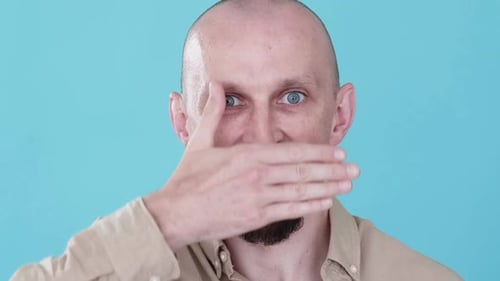 Man Covers Face With Hand on Blue Background