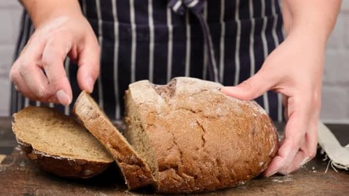Frau in einer blauen Schürze hält ein geschnittenes rundes Roggenbrot