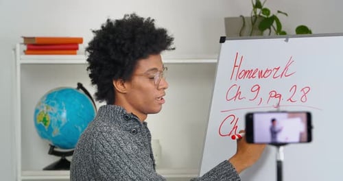 Curlyhaired Young Afro American Man Tutor Wears Glasses Stands at Blackboard Writes Talks Explains