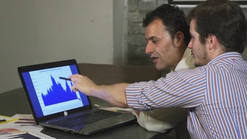 Two Men at Desk Looking at Computer Graph