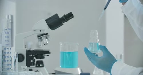 Lab Worker Using Pipette to Drop Liquid in Beaker