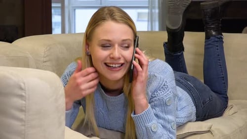 A Young Beautiful Woman Lies on a Couch and Talks on a Smartphone