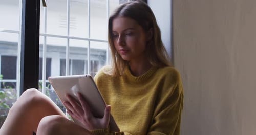 Woman using digital tablet while sitting near the window at home